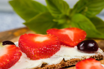 loaves with cheese, strawberries and cherries on a cutting board and gray background with mint leaves