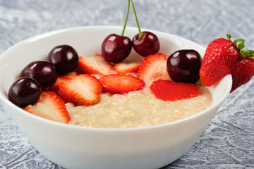 porridge in a white bowl with strawberries and cherries on a gray background