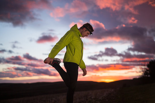 A male runner wearing a headlamp stretches after doing hill sprints at dusk in north Idaho.