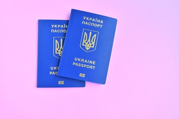 Two Biomedical Ukraine id passports on pink background with selective focus and empty space for photo or text. Ukrainian id passport with a golden symbol trident on neon backdrop. Copy space 
