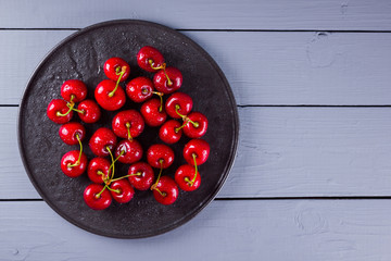Cherries on a gray background. Red cherries on black plate. Berries in drops of water on wooden boards. Healthy food. Copy space