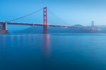 Obraz premium Classic panoramic view of famous Golden Gate Bridge seen from San Francisco harbour in beautiful evening light on a dusk with blue sky and clouds and fog in summer, San Francisco, California, USA
