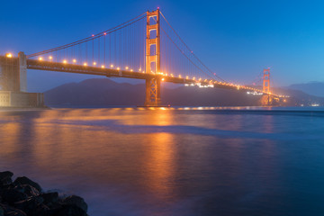 Classic panoramic view of famous Golden Gate Bridge seen from San Francisco harbour in beautiful evening light on a dusk with blue sky and clouds and fog in summer, San Francisco, California, USA