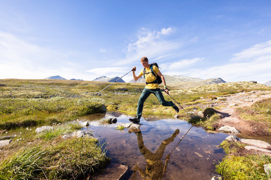 Rondane National Park, Norway: A male hiker crossing a little alpine stream near the Rondvassbu lodge.