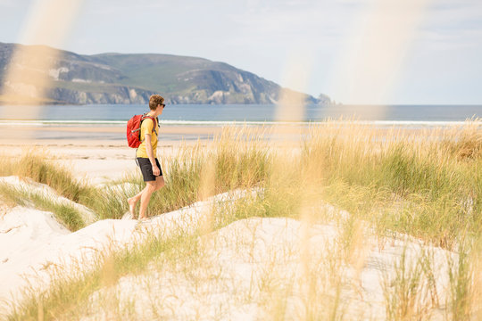 Tramore Beach, Kiltooris, Portnoo, Donegal, Ireland: A man walking thorugh the dunes by the beach.