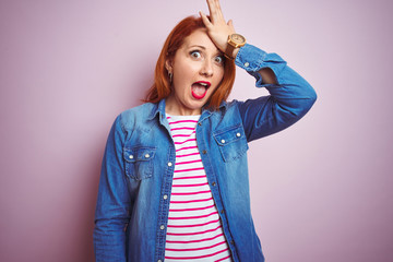 Beautiful redhead woman wearing denim shirt and striped t-shirt over isolated pink background...