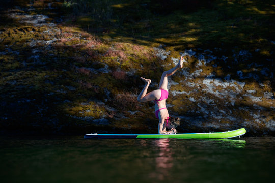 A woman does yoga on a stand up paddle board at sunset in Lake Pend Oreille in north Idaho in summer.