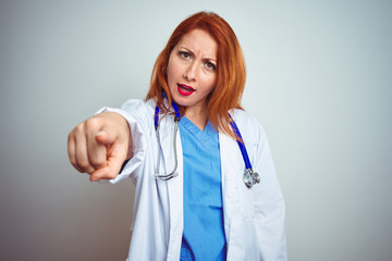 Young redhead doctor woman using stethoscope over white isolated background pointing displeased and frustrated to the camera, angry and furious with you