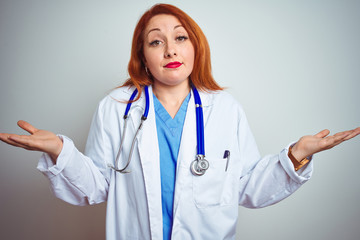 Young redhead doctor woman using stethoscope over white isolated background clueless and confused expression with arms and hands raised. Doubt concept.