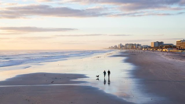 Aerial view of the beautiful sandy beach with a couple of people walking during a vibrant sunrise. Taken in Daytona Beach, Florida, United States. Still Image Continuous Animation