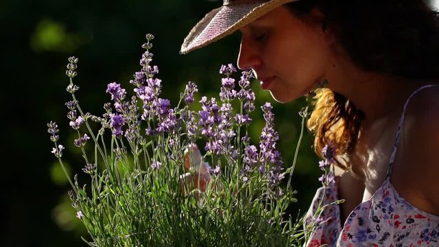 Woman sniffs lavender flowers and sprays lavender spray on herself.