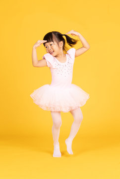 Cute Ballerina Little Asian Girl In Pink Dancer Over A Yellow Background. Kid In Dance Class. Child Girl Is Studying Ballet.