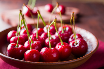Cherries on a clay plate. Sweet cherries on a wooden board. Red berries in drops of water on a red napkin. Rustic style. Copy space