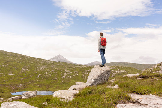 Glenveagh National Park, Donegal, Ireland:  A hiker standing on a rock overlooking the landscape and towards the Errigal Peak.