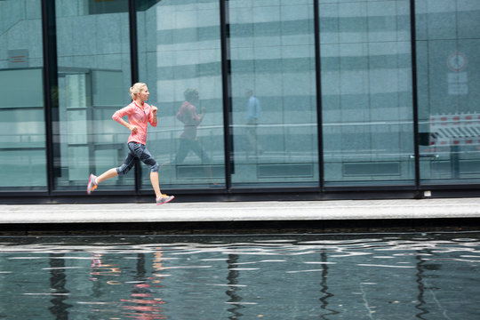  European Quarter, Stuttgart, Baden-W&cedil;rttemberg, Germany: A female runner running along the glass walls of an office building that shows her reflection.