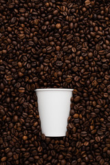 White disposable cup of coffee to go on the background of roasted beans.