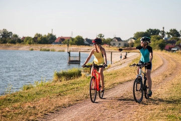 Fototapeta premium Women on bike riding by the lake shore outdoors at the park