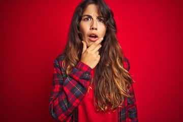 Young beautiful woman wearing casual jacket standing over red isolated background smiling swearing with hand on chest and fingers up, making a loyalty promise oath