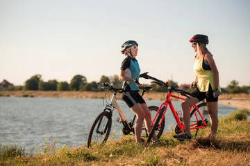 Two women cyclists with bikes standing and talking at the lake shore