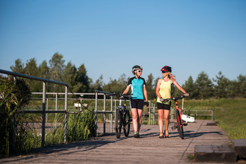 Obraz premium Two female friends walking with bikes and talking each other