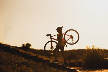 Fototapeta na wymiar Silhouette of a woman carrying a bike against evening sky