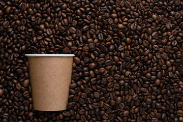 Craft disposable cup of coffee to go on the background of roasted beans.