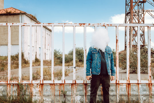 Man exhaling vape cloud in front of face while standing by fence