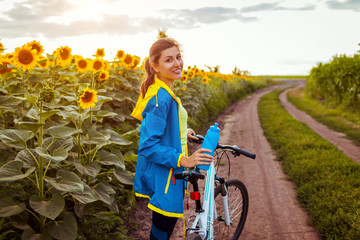 Young happy woman bicyclist riding bicycle in sunflower field. Summer sport activity. Healthy...