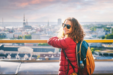 Young beautiful happy girl traveler on the viewing platform against the background of the old town of Riga, Latvia, travel to the Baltic countries - obrazy, fototapety, plakaty