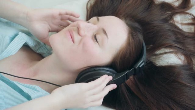 Woman lying on the bed listening to music with headphones and relaxes