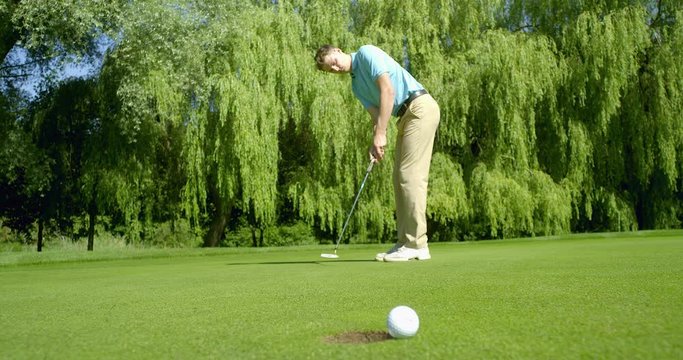 Unlucky!  A Golfer hits a putt as the golf ball rolls around the cup!