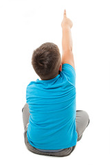 Back view of little boy sitting on floor, points at wall. Rear view. Isolated on white background 