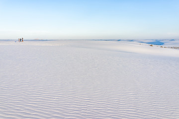 White sands dunes national monument gypsum sand and plants in New Mexico with horizon at sunset and people in distance