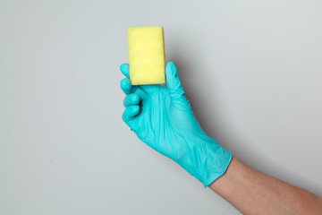 Hand in rubber glove holding cleaning sponge. Hand of chambermaid on gray background. Space for text.