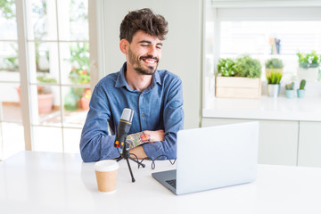 Fototapeta na wymiar Young man recording podcast using microphone and laptop looking away to side with smile on face, natural expression. Laughing confident.