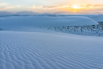 White sands dunes national monument pattern in New Mexico with sun over horizon at sunset with silhouette of Organ Mountains