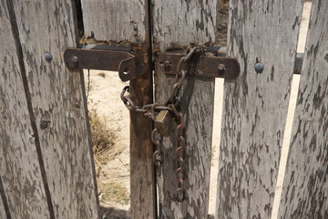 Wooden weathered old gate locked with rusty chain and lock.