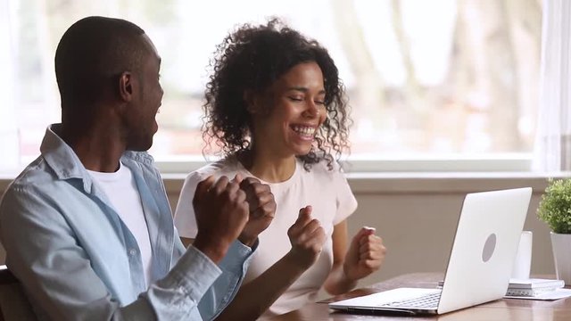 Euphoric african couple looking at laptop excited by online win