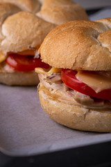 Two homemade burger Vienna Kaiser bread bun bread roll with chicken meat tomato mustard mayonnaise on baking tray sheet parchment paper white background