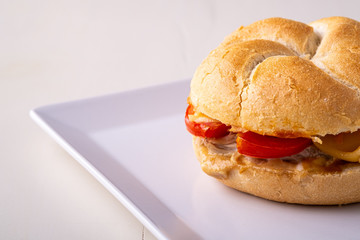 Single homemade burger Vienna Kaiser bread bun bread roll with chicken meat tomato mustard mayonnaise on white square plate background