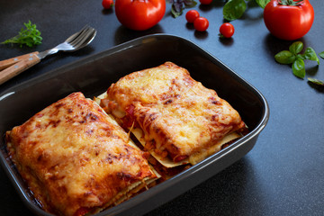Homemade Italian Lasagna with Tomato Sauce, Tomatoes and Basil. Two portions. Close-up. Dark background