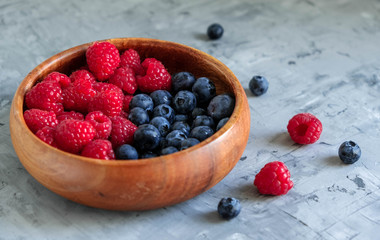 Fresh blueberries and raspberries in a wooden eco-friendly plate on a gray background. Raw foods, vegetarianism. Healthy food and diet