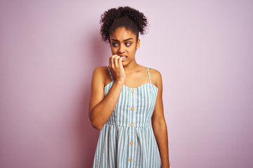 African american woman wearing casual striped dress standing over isolated pink background looking stressed and nervous with hands on mouth biting nails. Anxiety problem.