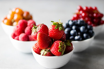 Fresh berries in white bowls on a gray background. Blueberries, strawberry, raspberry, gooseberries and redcurrants.