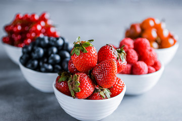 Fresh berries in white bowls on a gray background. Blueberries, strawberry, raspberry, gooseberries and redcurrants.