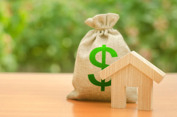 Wooden house figurine and money bag on the background of nature. Mortgage loan for the purchase of...
