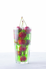 Cherry cocktail. Red cherries in a glass on a white background. Green carbonated drink with sweet cherries. Copy space