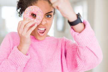 Young african american girl eating sweet pink donut annoyed and frustrated shouting with anger, crazy and yelling with raised hand, anger concept