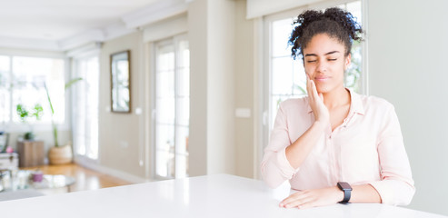 Wide angle of beautiful african american woman with afro hair touching mouth with hand with painful expression because of toothache or dental illness on teeth. Dentist concept.