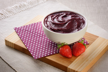 Açaí bowl with strawberries under napkin and wood board